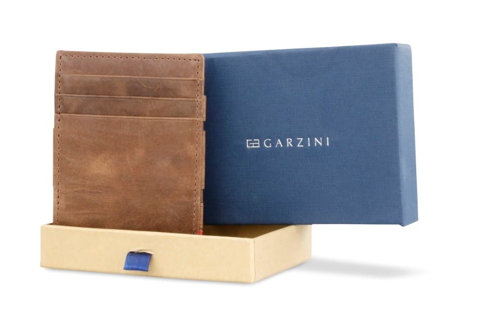 Half-open blue box with Garzini brand name Inside the box, the Brushed Brown wallet is wrapped in tissue paper, placed in a light cardboard box with a blue strap.